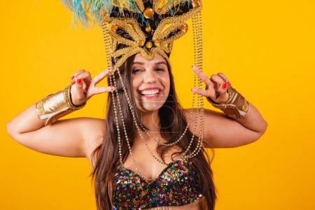 Photo for Beautiful Brazilian woman in golden carnival clothes, wearing carnival dancer feather crown. peace and love, pose for selfie. - Royalty Free Image