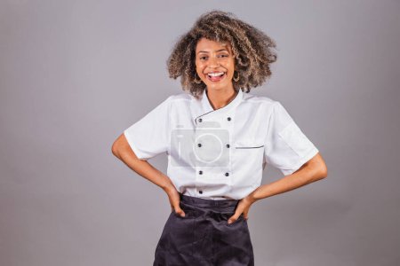 Téléchargez les photos : Jeune Brésilienne noire, cuisinière, chef cuisinière, portant l'uniforme de restaurant. Mains sur les hanches. - en image libre de droit