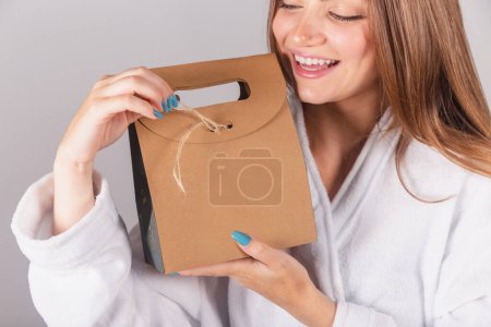 Photo for Brazilian blonde woman showing wonderful hair. dressed in a robe. holding cardboard bag with cosmetics and hair, close-up shot. - Royalty Free Image