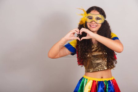 Foto de Jovencita adolescente, brasileña, con ropa frevo, carnaval. máscara, signo del corazón con las manos. - Imagen libre de derechos