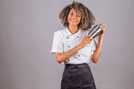Foto de Joven brasileña negra, cocinera, masterchef, vistiendo uniforme de restaurante. coctelera para preparar bebidas. - Imagen libre de derechos