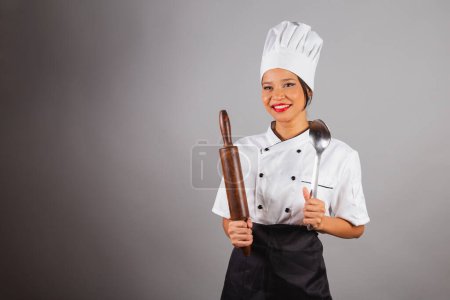 Téléchargez les photos : Chef cuisinier, cuisinier brésilien, du Nord-Est, tenant un rouleau à pâtisserie en bois pour la préparation du pain et des pâtes. Et cuillère en métal. - en image libre de droit