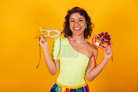 Foto de Hermosa mujer brasileña afroamericana, en ropas de carnaval, sosteniendo dos máscaras de carnaval. - Imagen libre de derechos