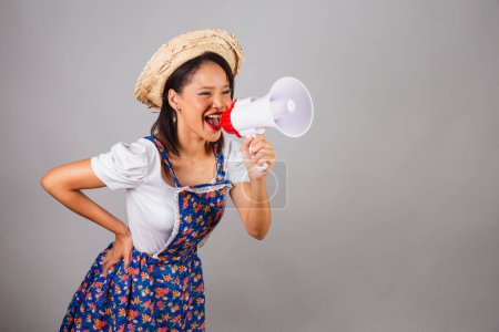 Photo for Brazilian woman, northeastern, with June party clothes, straw hat. using mega phone for advertising promotion, advertisement, marketing. - Royalty Free Image