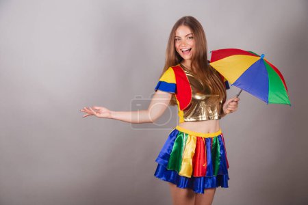 Foto de Mujer rubia brasileña vestida con ropa frevo, carnaval. con colorido paraguas frevo. mostrando algo a la izquierda. - Imagen libre de derechos