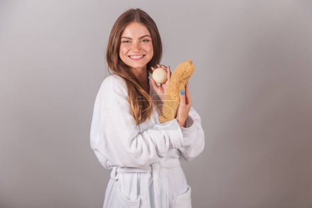 Téléchargez les photos : Belle femme brésilienne vêtue de peignoir, tenant du savon et du loofah naturel pour les soins de la peau. exfoliation. - en image libre de droit