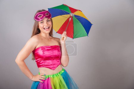 Foto de Mujer rubia brasileña vestida con ropa de carnaval rosa. con una máscara, con un paraguas frevo. - Imagen libre de derechos
