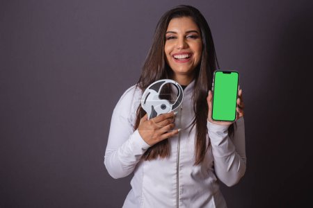Photo for Horizontal photo. brazilian woman with medical coat, nutritionist. adipometer and smartphone, green screen. slimming. - Royalty Free Image