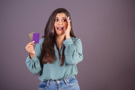 Photo for Horizontal photo. Beautiful Brazilian woman, with casual clothes, Jeans and green shirt. holding credit cards. Expressions. - Royalty Free Image