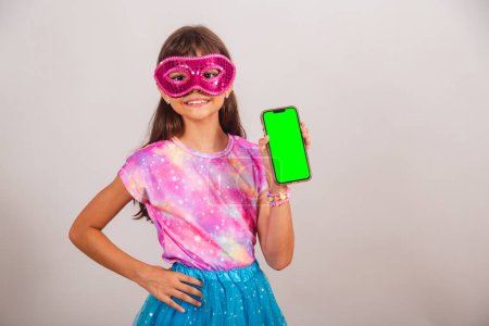 Téléchargez les photos : Belle fille brésilienne, enfant, habillée pour le carnaval au Brésil. mains sur la taille avec smartphone avec écran Chroma vert. - en image libre de droit