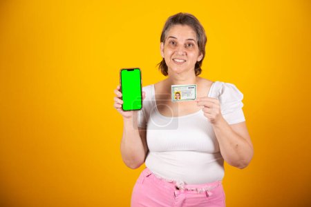 Photo for Adult Brazilian woman holding identity card, ID card and smartphone with green screen - Royalty Free Image