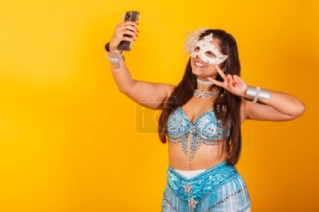 Téléchargez les photos : Belle femme brésilienne en bleu et blanc vêtements de carnaval. tenant smartphone prenant autoportrait. - en image libre de droit