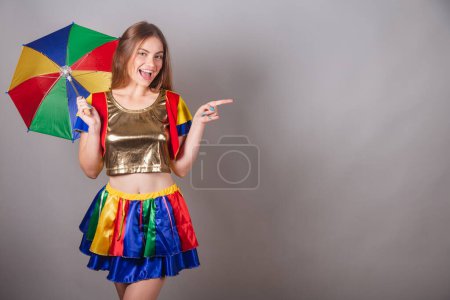 Foto de Mujer rubia brasileña vestida con ropa frevo, carnaval. con colorido paraguas frevo. mostrando algo a la derecha. - Imagen libre de derechos