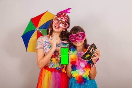Photo for Two brazilian children, girls, friends, dressed in carnival clothes, holding smartphone, app, mobile. - Royalty Free Image
