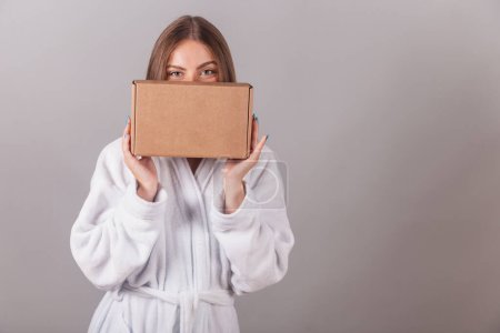 Photo for Brazilian blonde woman showing wonderful hair. dressed in a robe. holding medium cardboard box with cosmetics. - Royalty Free Image