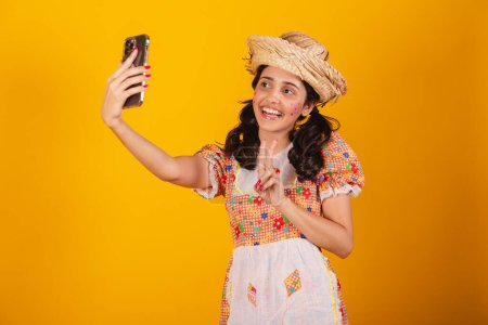 Photo for Beautiful brazilian woman, with festa junina clothes, taking self portrait with smartphone. - Royalty Free Image