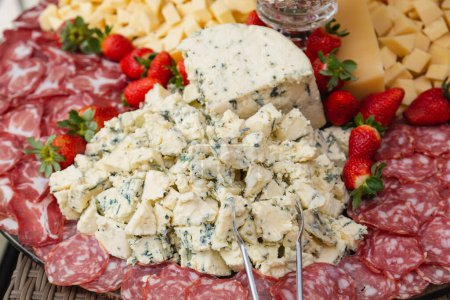 Photo for Gorgonzola cheese in focus, on a charcuterie board, next to strawberries and salami. - Royalty Free Image