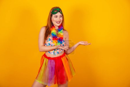 Téléchargez les photos : Belle fille brésilienne aux cheveux roux en vêtements de carnaval présentant quelque chose à droite. - en image libre de droit