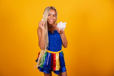 Foto de Hermosa mujer negra, brasileña con trenzas, con ropa para el carnaval. Moneda de retención y alcancía. - Imagen libre de derechos