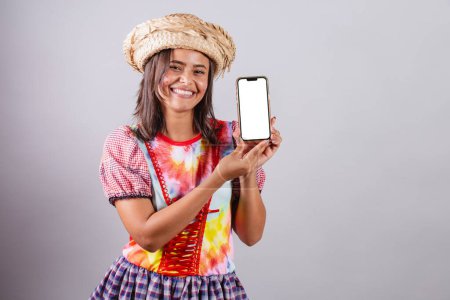 Foto de Mujer brasileña vistiendo ropa de campo, fiesta So Joo, fiesta Junina. Con smartphone mostrando pantalla blanca en croma - Imagen libre de derechos