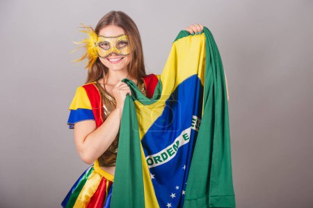 Téléchargez les photos : Femme blonde brésilienne, vêtue de vêtements frevo, masque de carnaval, tenant le drapeau du Brésil. - en image libre de droit