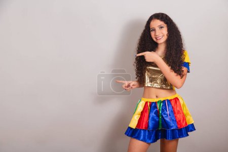 Téléchargez les photos : Jeune adolescente, brésilienne, avec des vêtements frevo, carnaval. présenter quelque chose sur le côté, la publicité. - en image libre de droit