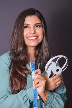 Photo for Horizontal photo. Beautiful Brazilian woman, with casual clothes, Jeans and green shirt. nutritionist holding measuring tape and adipometer - Royalty Free Image