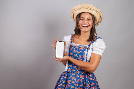 Foto de Mujer brasileña vistiendo ropa de campo, fiesta So Joo, fiesta Junina. con smartphone y pantalla para publicidad y publicidad. - Imagen libre de derechos
