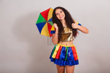 Téléchargez les photos : Jeune adolescente, brésilienne, avec des vêtements frevo, carnaval. avec parapluie comme signe avec les doigts. - en image libre de droit