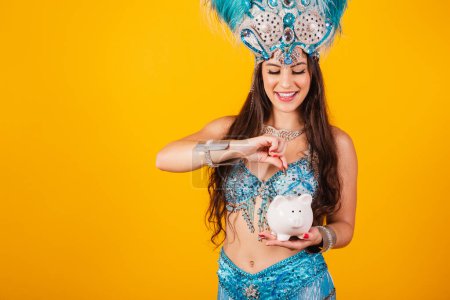 Photo for Beautiful brazilian woman with queen clothes from samba school, carnival. Feather crown, holding piggy bank and coin. - Royalty Free Image