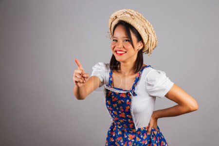 Photo for Brazilian woman, northeastern, with June party clothes, straw hat. pointing at something in the distance. - Royalty Free Image