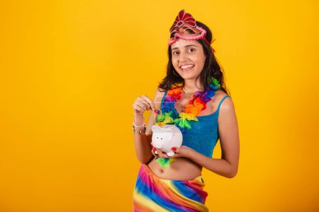 Photo for Beautiful brazilian woman in carnival clothes holding piggy bank and coin. - Royalty Free Image