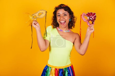 Foto de Hermosa mujer brasileña afroamericana, en ropas de carnaval, sosteniendo dos máscaras de carnaval. - Imagen libre de derechos