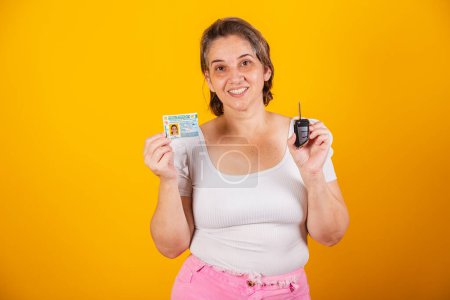 Photo for Adult Brazilian woman holding car key and driver's license. - Royalty Free Image