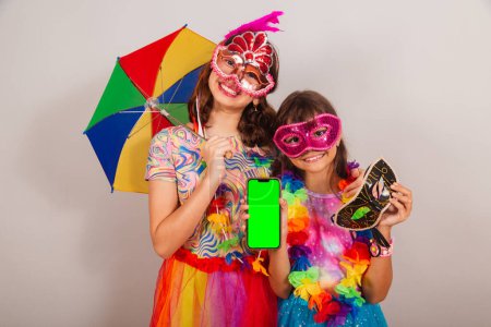 Foto de Dos niños brasileños, niñas, amigos, vestidos con ropa de carnaval, sosteniendo el teléfono inteligente, aplicación, móvil. - Imagen libre de derechos