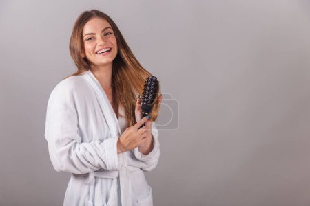 Photo for Brazilian blonde woman showing wonderful hair. dressed in a robe. using hairbrush. - Royalty Free Image