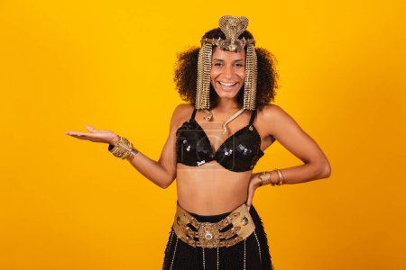 Foto de Hermosa brasileña negra, vestida con ropa de carnaval Cleopatra, presentando algo a la izquierda. - Imagen libre de derechos