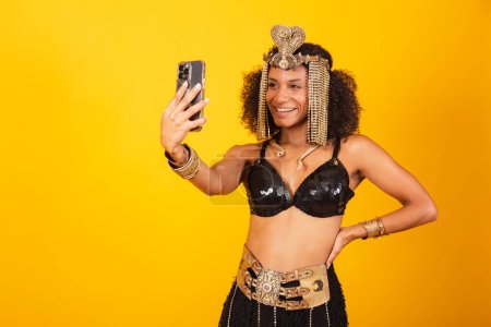 Téléchargez les photos : Belle femme brésilienne noire, en vêtements de carnaval Cleopatra, prenant autoportrait avec smartphone - en image libre de droit