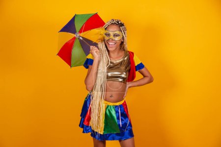 Foto de Hermosa mujer brasileña negra, vestida con ropa de carnaval, máscara. fondo amarillo. sosteniendo paraguas frevo. - Imagen libre de derechos