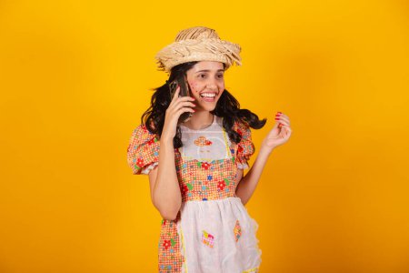 Foto de Mujer brasileña hermosa, con ropa de fiesta de junio, hablando en llamada de voz por teléfono inteligente. - Imagen libre de derechos