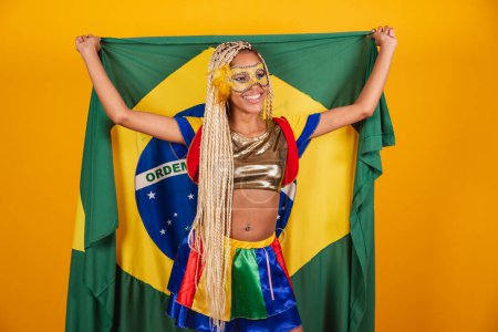 Téléchargez les photos : Belle femme brésilienne noire, vêtue de vêtements de carnaval, masque. fond jaune. tenant le drapeau brésilien. - en image libre de droit