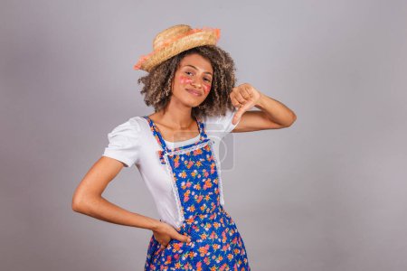 Photo for Young black Brazilian woman, with country clothes, dressed for Festa Junina. Saint John's festival. Thumb down, negative, frustrated, disapproving. - Royalty Free Image