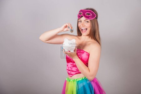 Photo for Brazilian blonde woman dressed in pink carnival clothes. holding piggy bank and coin. Save money. invest. - Royalty Free Image