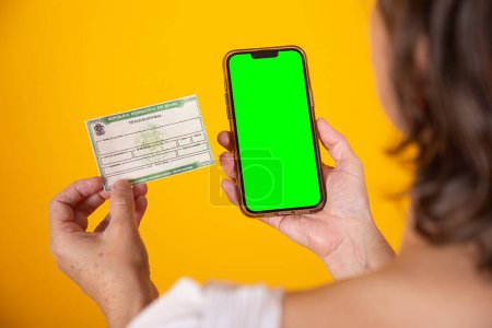 Photo for Hand holding Brazilian voter registration card and smartphone with green screen - Royalty Free Image