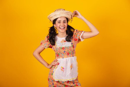 Téléchargez les photos : Belle femme brésilienne, avec des vêtements de fête de juin, posant pour une photo avec sa main sur son chapeau. - en image libre de droit