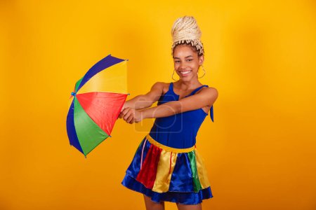 Photo for Beautiful black Brazilian woman, dressed in carnival clothes, blue, and yellow background, bun and braids, frevo umbrella. - Royalty Free Image
