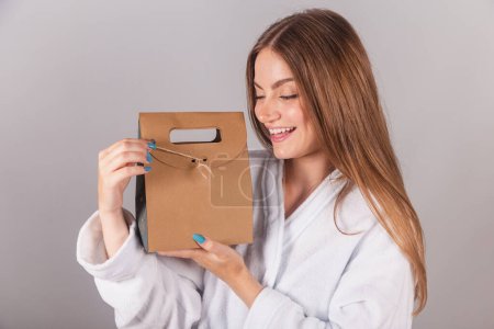 Photo for Brazilian blonde woman showing wonderful hair. dressed in a robe. holding cardboard bag with cosmetics and hair, close-up shot. - Royalty Free Image