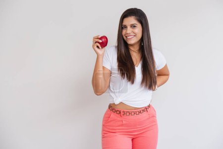 Téléchargez les photos : Belle femme brésilienne, chemise blanche et pantalon rose. photo publicitaire, manger de la pomme. - en image libre de droit