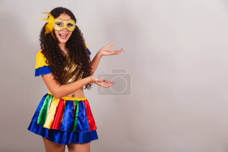 Téléchargez les photos : Jeune adolescente, brésilienne, avec des vêtements frevo, carnaval. mascara, montrant le produit sur le côté. - en image libre de droit