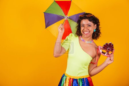 Téléchargez les photos : Belle femme brésilienne afro-américaine, vêtue de carnaval, acclamant, utilisant un parasol coloré. et masque de carnaval. - en image libre de droit